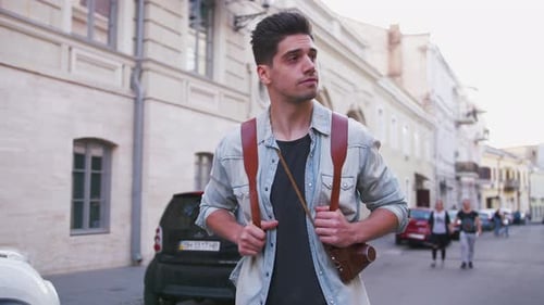 Attractive Young Handsome Man Tourist with Backpack Walking in City Center and Looking Around Slow