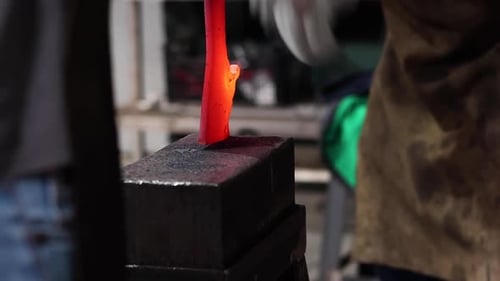Blacksmiths forging hot metal with hammer in workshop