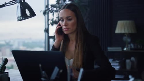 Businesswoman Talking on Smartphone in Office. Woman Looking at Laptop Screen