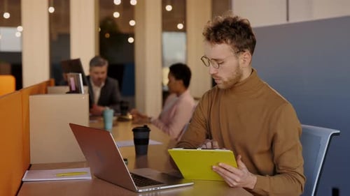 Beschäftigter kaukasischer Mann schaut auf das Tablet und tippt auf die Tastatur, während er im Büro sitzt und