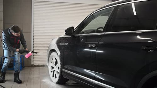 Man Washing Black SUV With Foam Cannon Indoors