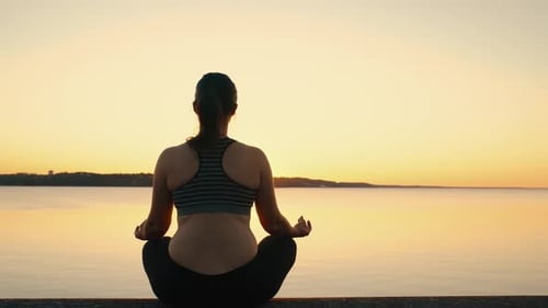 The Girl Meditates in the Lotus Position on the Lake at Sunset