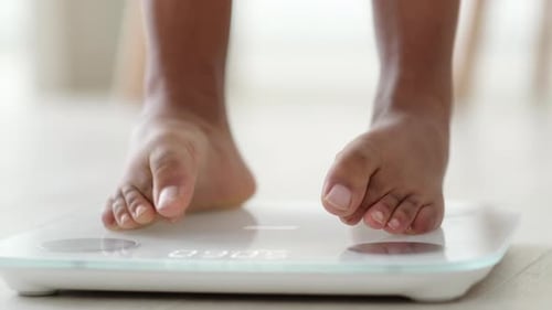 Legs of Black Girl Standing on Scale to Measure Weight
