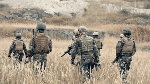 Soldiers Walking Armed Through Grassy Rural Field