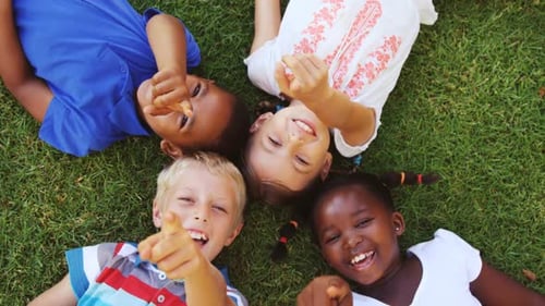 Smiling Children Laying on the Grass Pointing Upward