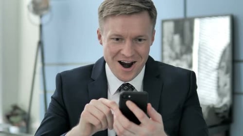 Man Celebrates While Using Smartphone in Office