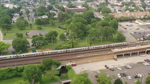 An aerial shot of a train leaving the station on a cloudy day in the evening. The drone camera dolly