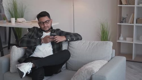 Young Adult Relaxing with Mobile Phone on Sofa