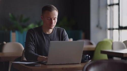 Handsome Freelancer Businessman in Glasses Diligently Working on Laptop in Cafe