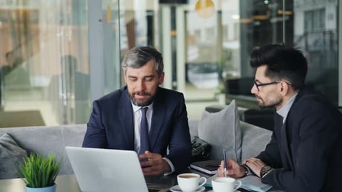 Mature Businessmen Talking in Cafe Looking at Laptop Screen Discussing Contract