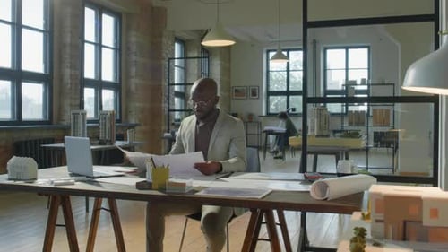 African American Architect Examining Paper Plans in Office