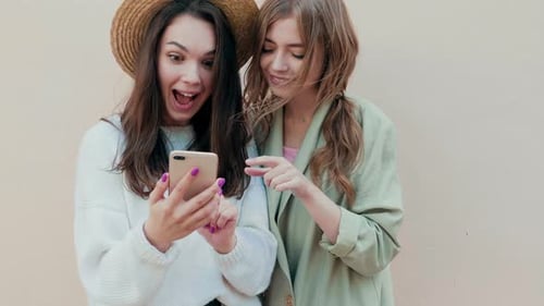Two Young Women Looking at Smartphone and Laughing