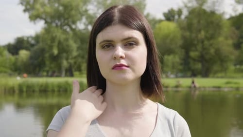 A Young Caucasian Woman Looks Seriously at the Camera in a City Park Closeup