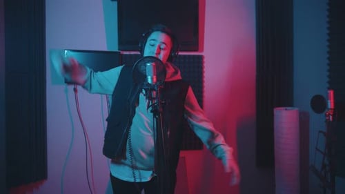 A Man in Hoodie Rapping in the Studio Gesticulates While Recording His Track