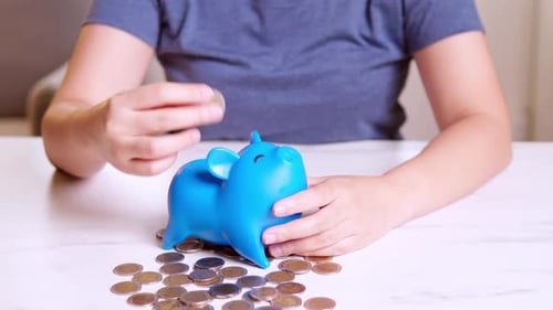 Woman makes savings puts money in a piggy bank. Woman is putting coins into piggy bank.