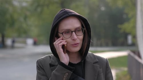 Woman in Hoodie Talks on Cell Phone in Park