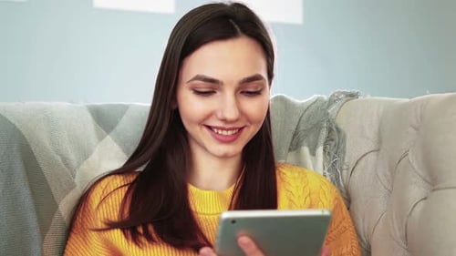 Woman Smiling Using Tablet Device on Couch at Home