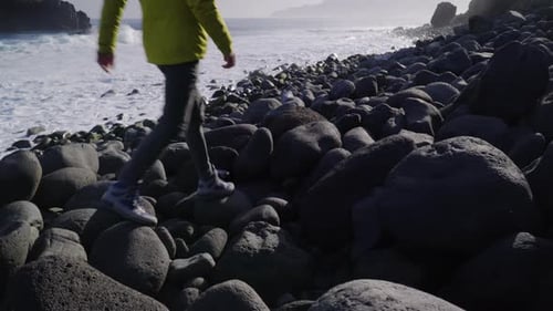 Young man walking on the rocky ocean coast at the sunrise