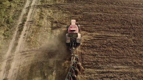 Tracteur puissant équipé d'une charrue cultivant le champ et soulevant d'énormes nuages de poussière brune suffocante