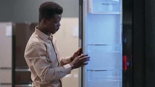 Male Afroamerican Visitor is Choosing New Refrigerator in Home Appliance Store Viewing Exhibition