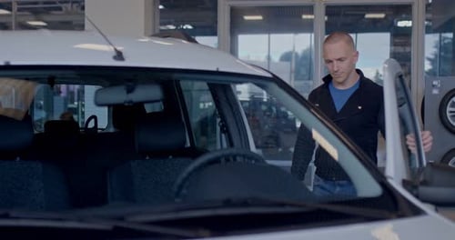 Feliz comprador masculino abre a porta e entra em um carro novo comprando em um salão de automóveis