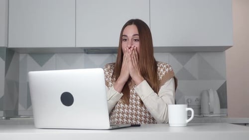 Woman Expressing Surprise While Using Laptop in Kitchen