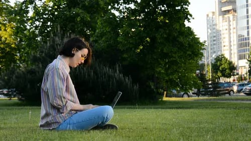 Young Brunette Woman Sitting on Green Grass and Use Laptop