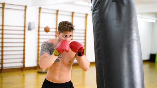 Young guy trains in a gym and fists his boxing bag fist