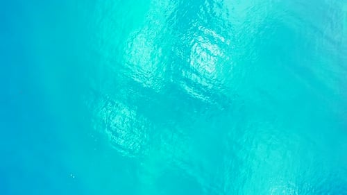 Glassy sea texture with turquoise water reflecting sunlight, copy space with abstract patterns on tr