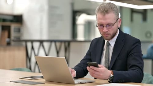 Professional Businessman Using Smartphone and Laptop in Office