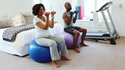 Couple Exercising with Dumbbells on Exercise Balls at Home