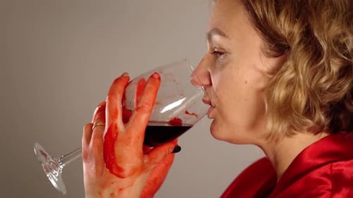 Mujer bebe vino tinto de vidrio manchado con sangre primer plano