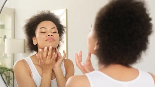 Woman Applying Skincare Product Looking in Mirror