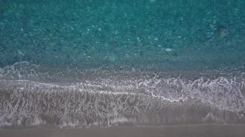 Türkisfarbene Wellen aus der Luft brechen am leeren Kiesstrand. Reines ruhiges Meer aus der Vogelperspektive