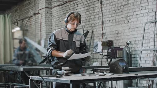 Young Man in Protective Glasses Working at the Plant Riding the Instruction on the Piece of Paper