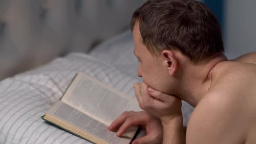 Young man reads a book before going to bed lying in bed