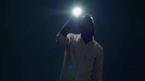 Young Person Sitting in the Dark and Using Flashlight to Search Around