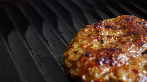 The fried cutlet for hamburger rotates on the grill pan.