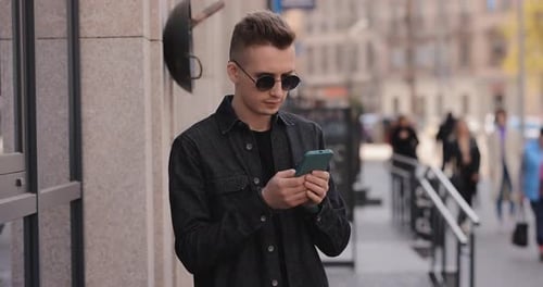 Young Man in Sunglasses Using Phone in a City