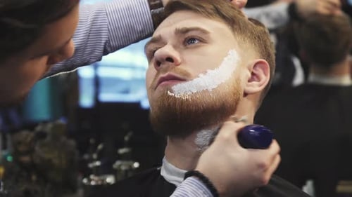 Barbier, der Rasiercreme auf den Bart seines Kunden aufträgt