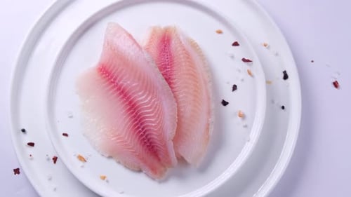 Fillet of Telapia Fish or Other Sea Fish Closeup on a Plate with Spices and Salt