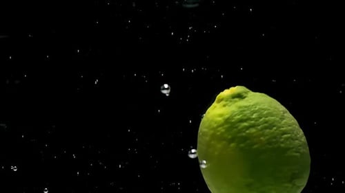 Green Lime Fruit Falls Down Into Water on Black Background