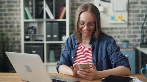 Woman Using Smartphone at Desk with Laptop