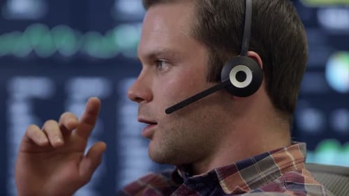 Side view of man talking on headset in front of computer screen.