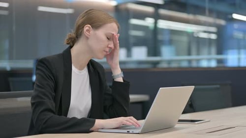Woman Massaging Temples in Office with Laptop
