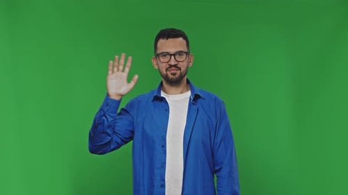 Man Waves His Hand at the Camera While Standing on the Background of a Green Chroma Key