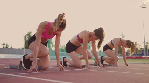 Three Young Women in the Stadium on the Start Line in Blocks Start in the Race in Slow Motion