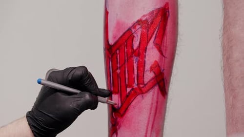 Tattoo Artist Adding Finishing Touches to a Sketch with Letters on the Leg on His Client with a Pen