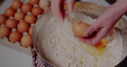 Hands Cracking Eggs Into Bowl of Flour