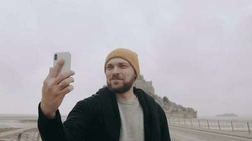 Happy Young Excited Caucasian Blogger Man Filming Smartphone Selfie Video of Epic Mont Saint Michel